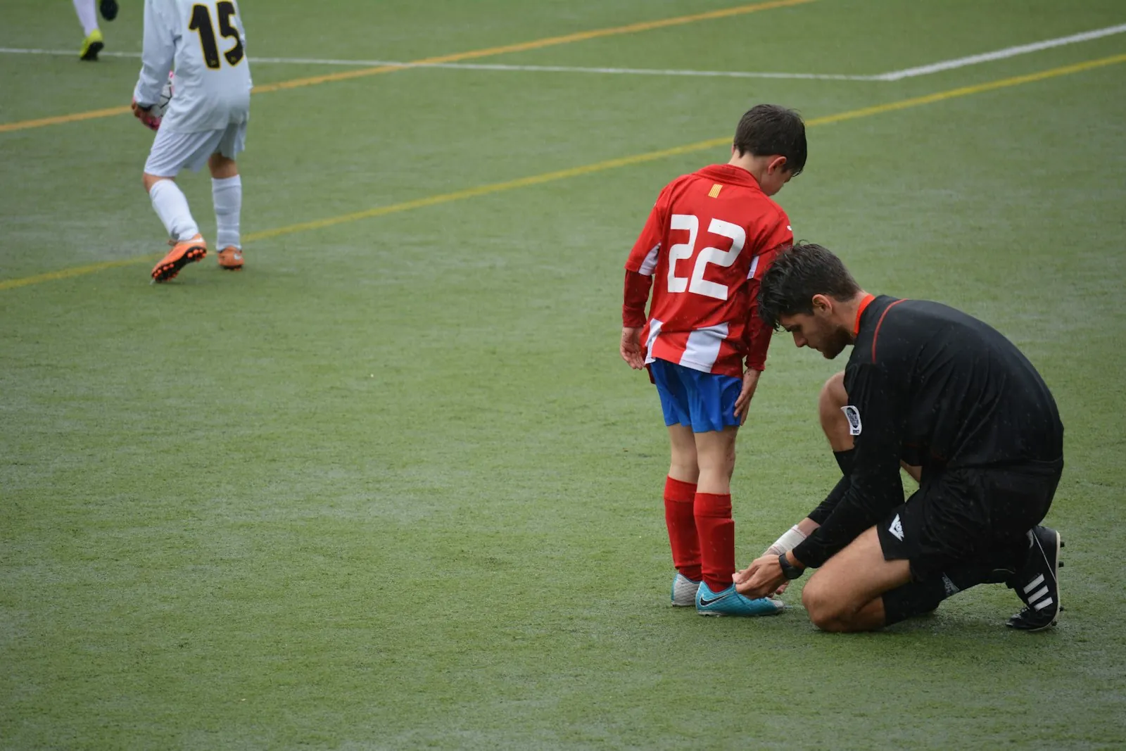 A football coach kneeling to tie a young player's boot during training