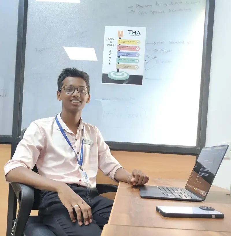 Rahul at his first workspace: a MacBook and an iPhone on a desk, a goals poster on the whiteboard behind him