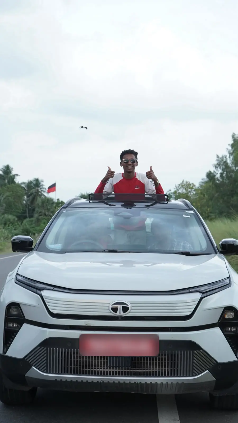 Rahul standing out of a car sunroof on a country road, giving two thumbs up