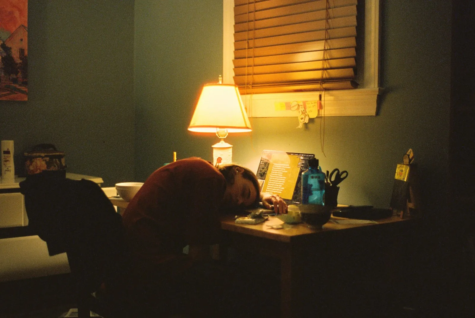 A person asleep at a desk under a warm lamp