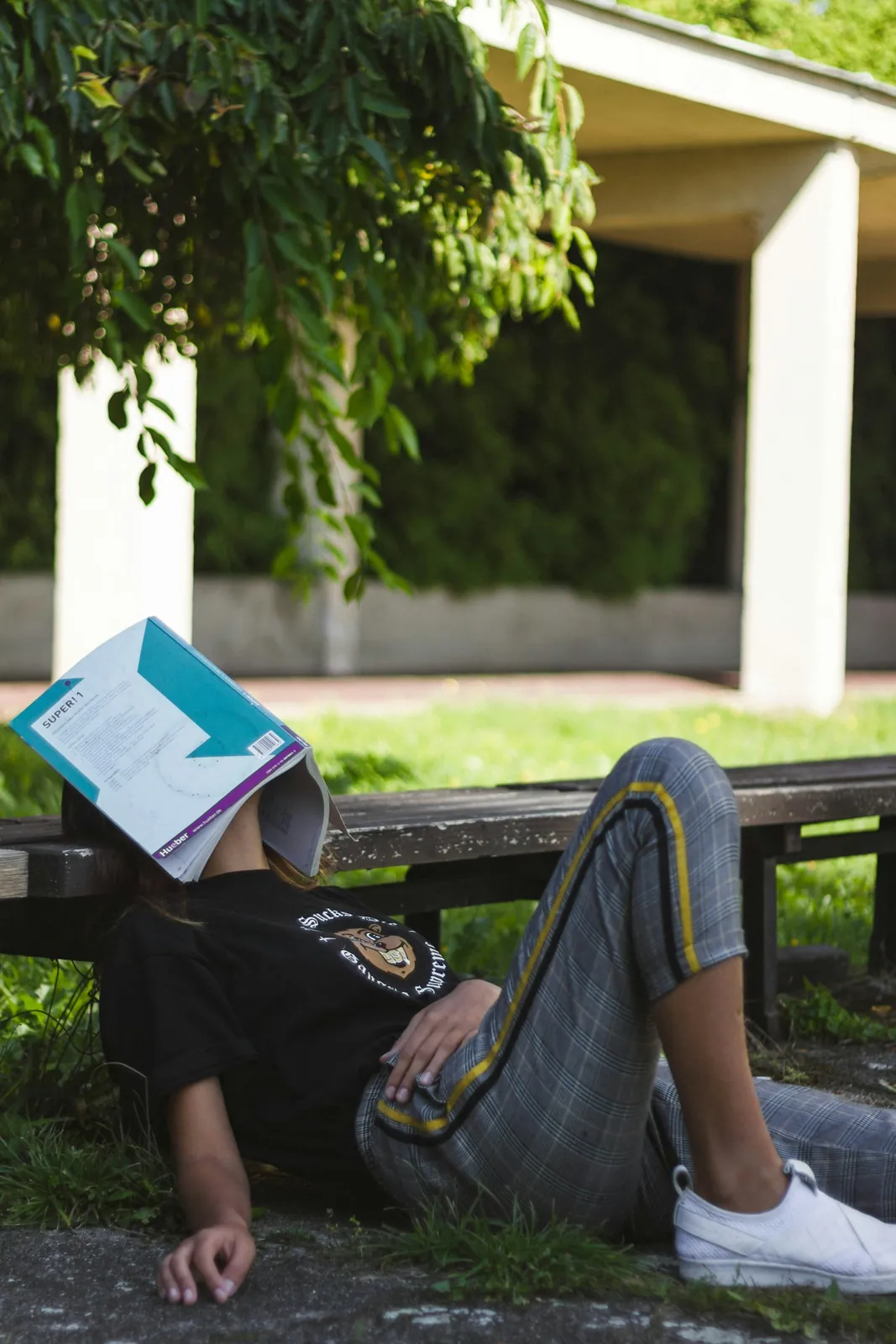 A tired student lying on a bench with a textbook over their face