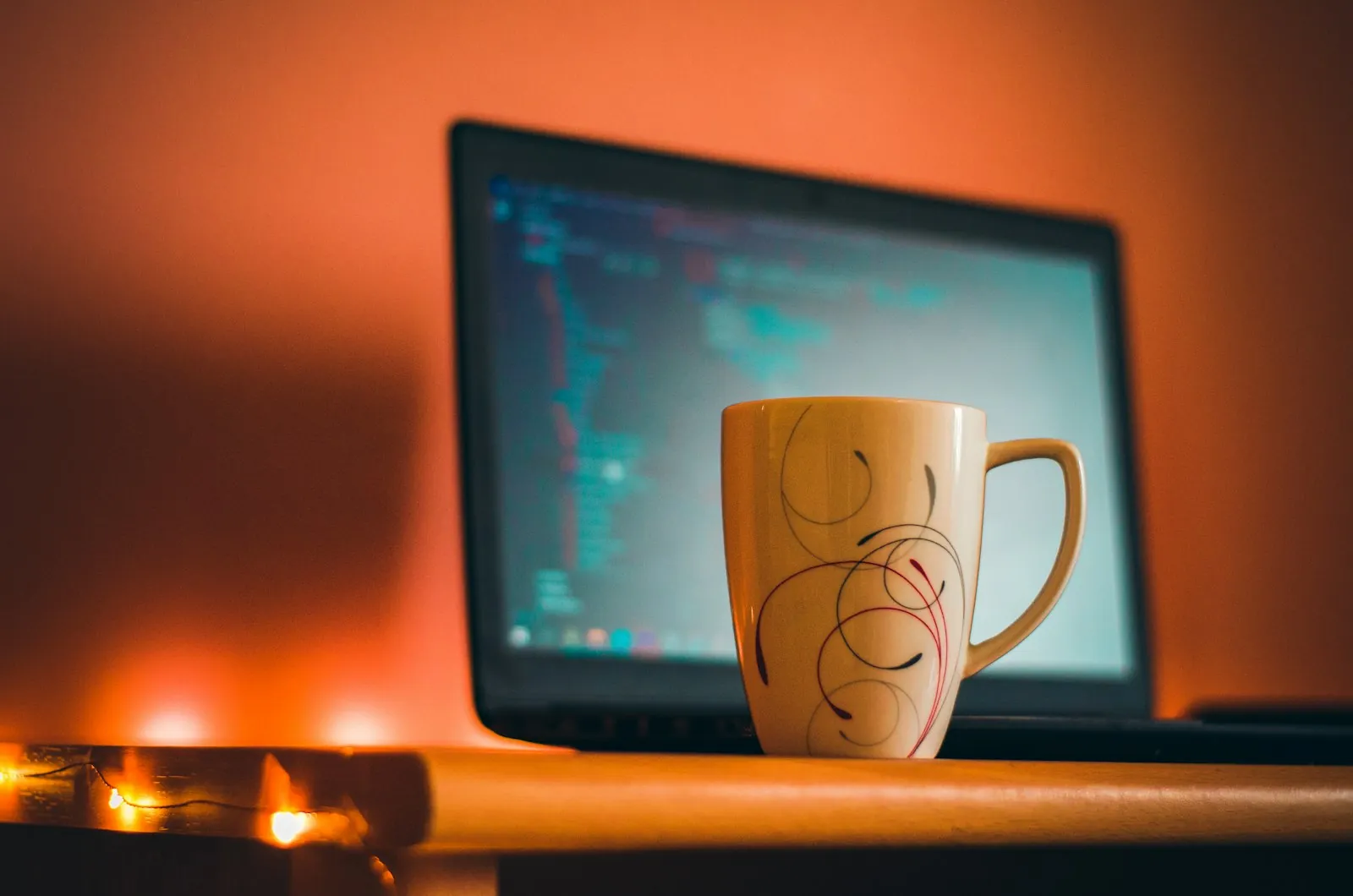 A coffee mug sits in front of a laptop showing code, lit by warm orange light late at night