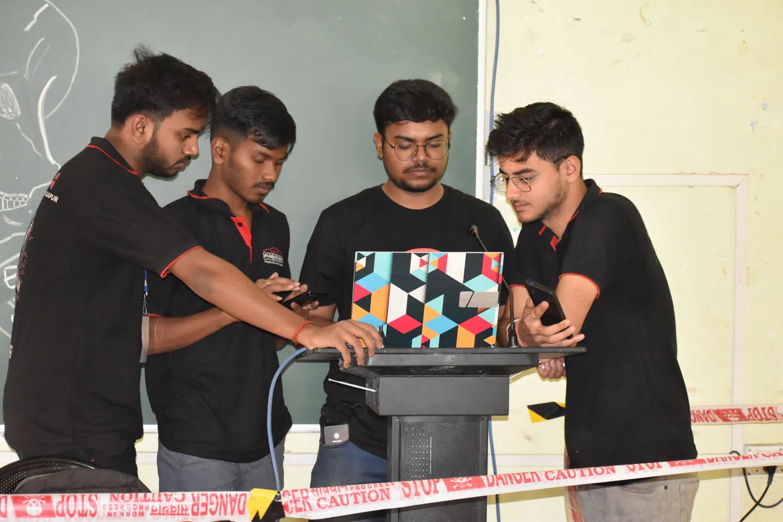 Four college students crowd around a laptop on a podium as they get their project demo ready