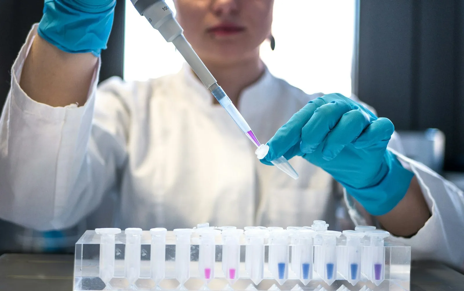 A scientist using a pipette over test tubes in a research lab