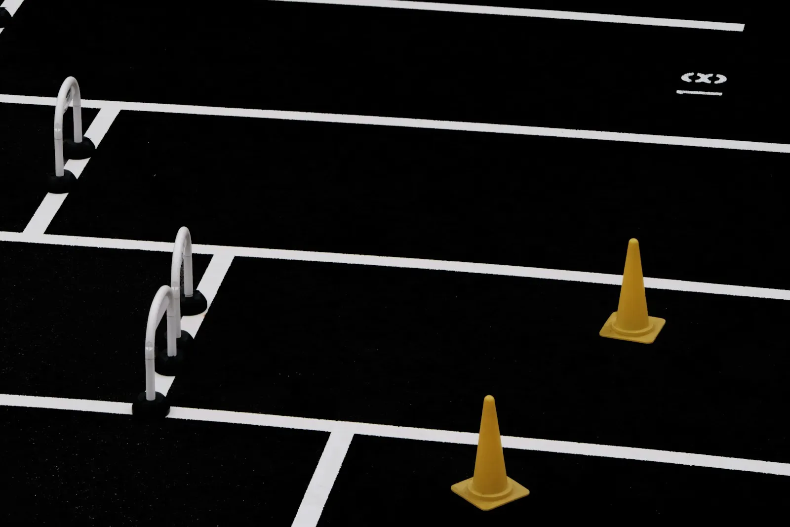 Training lanes marked with white lines on a black surface, with white hurdles and yellow cones in separate lanes