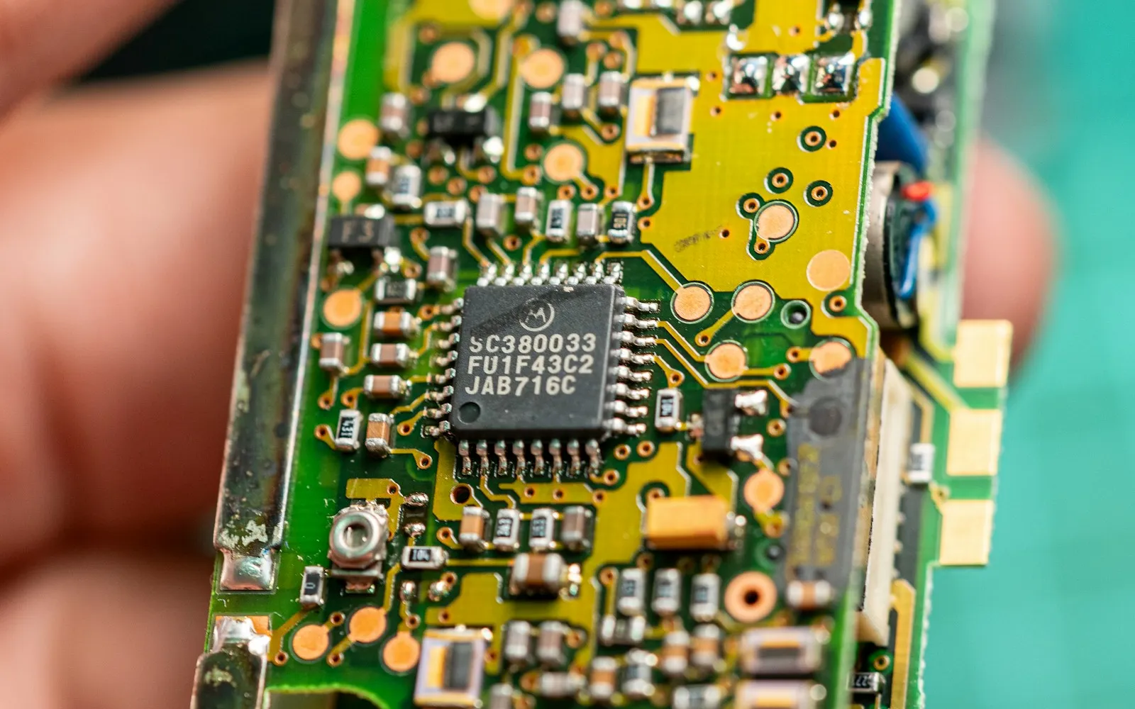 A small circuit board with a Motorola chip, held between finger and thumb
