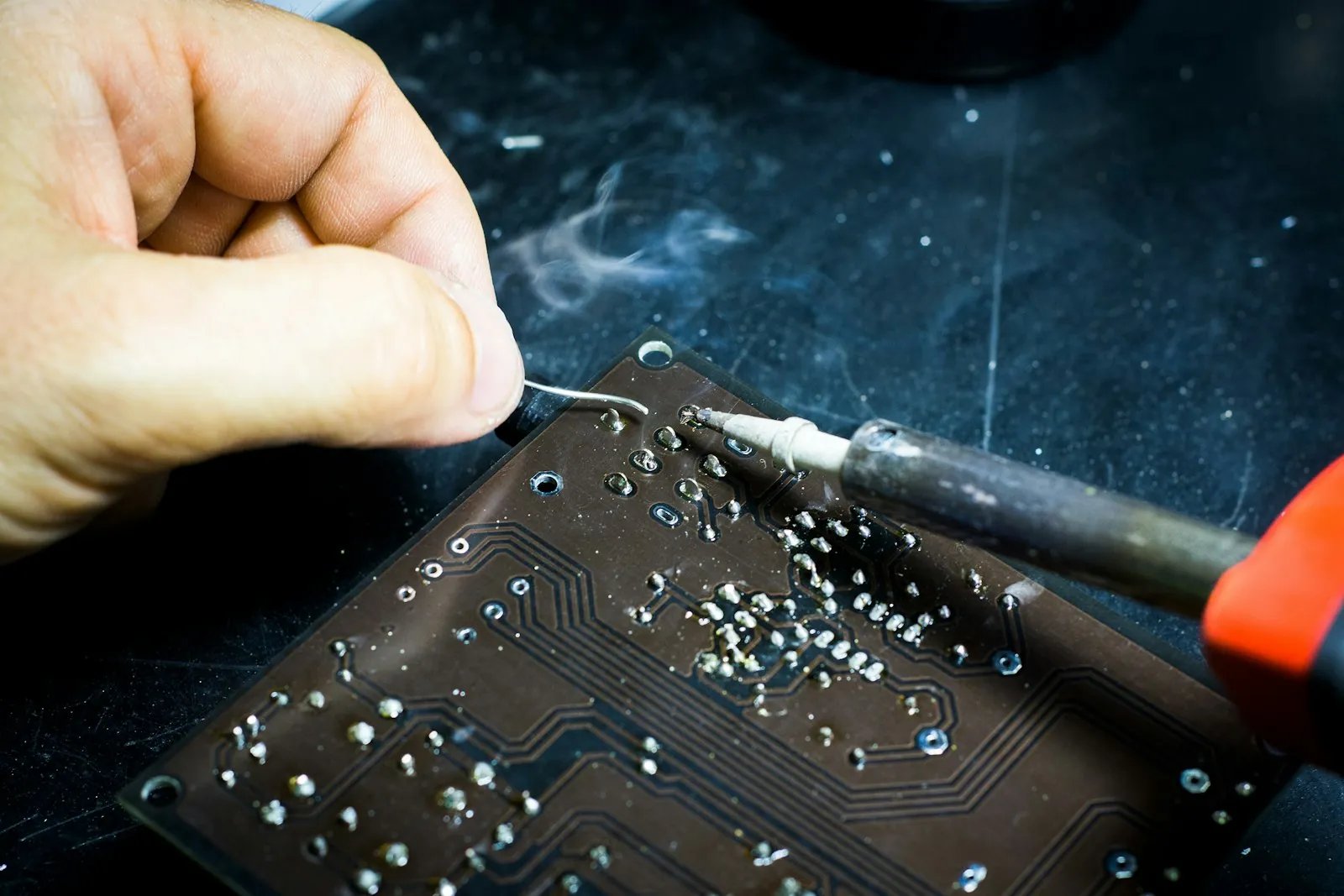 Soldering iron tip joining components on a printed circuit board while a hand feeds solder wire