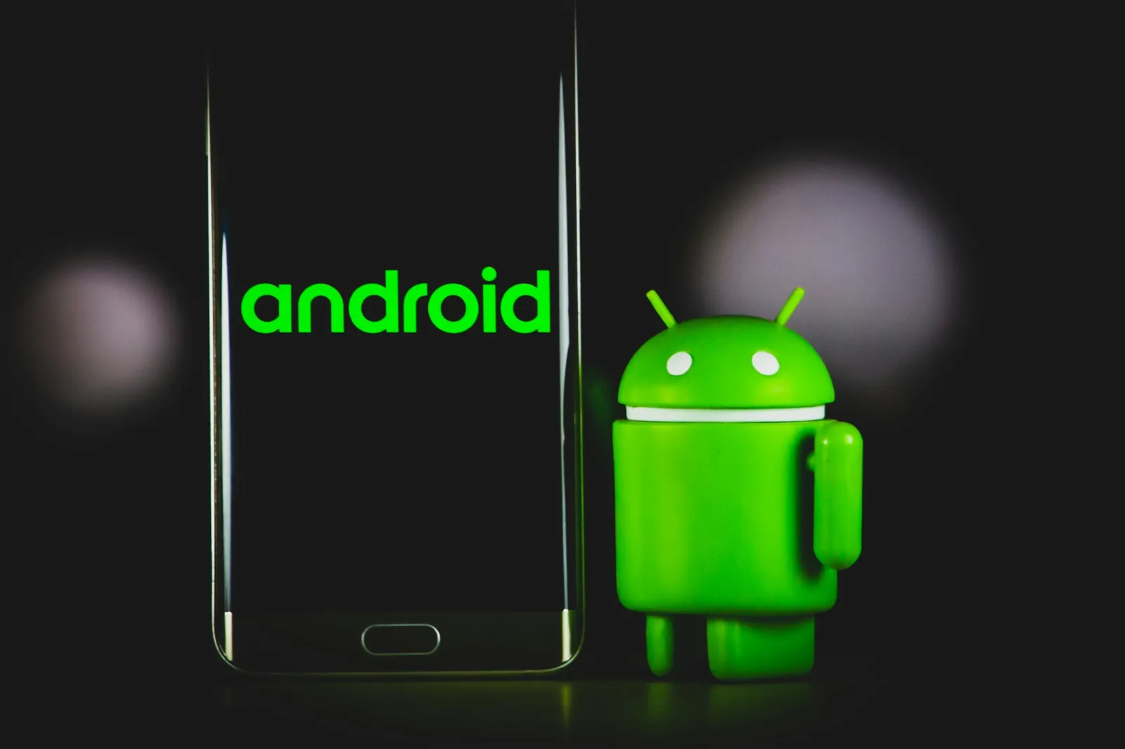 A smartphone showing the word android next to a small green Android robot figure, on a dark background