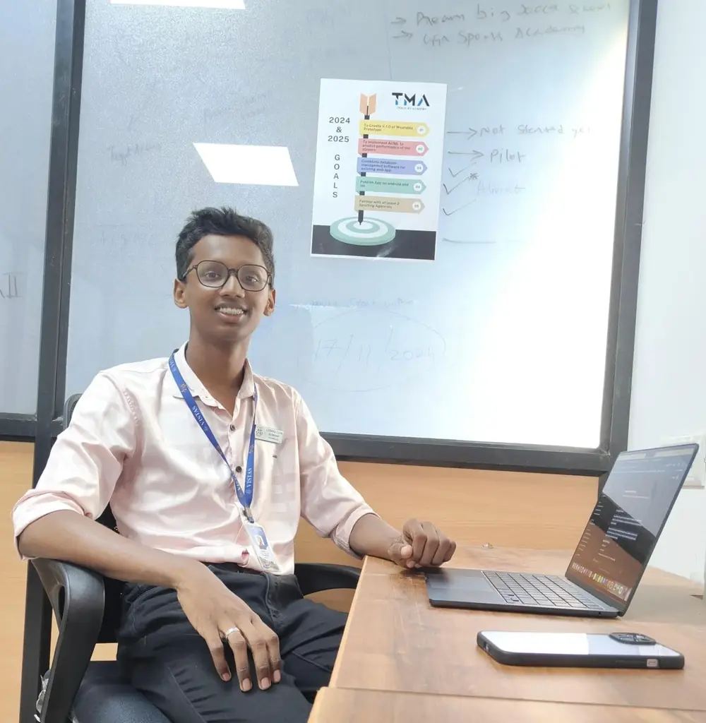 Rahul at his first workspace with a MacBook and an iPhone, the Track My Academy goals poster behind him
