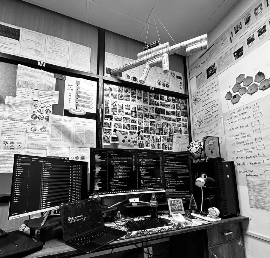 The office desk: three monitors, a Pikachu, a goals poster and a chandelier made of Monster cans