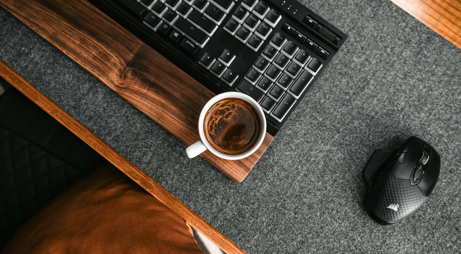 A cup of coffee next to a computer keyboard on a wooden desk