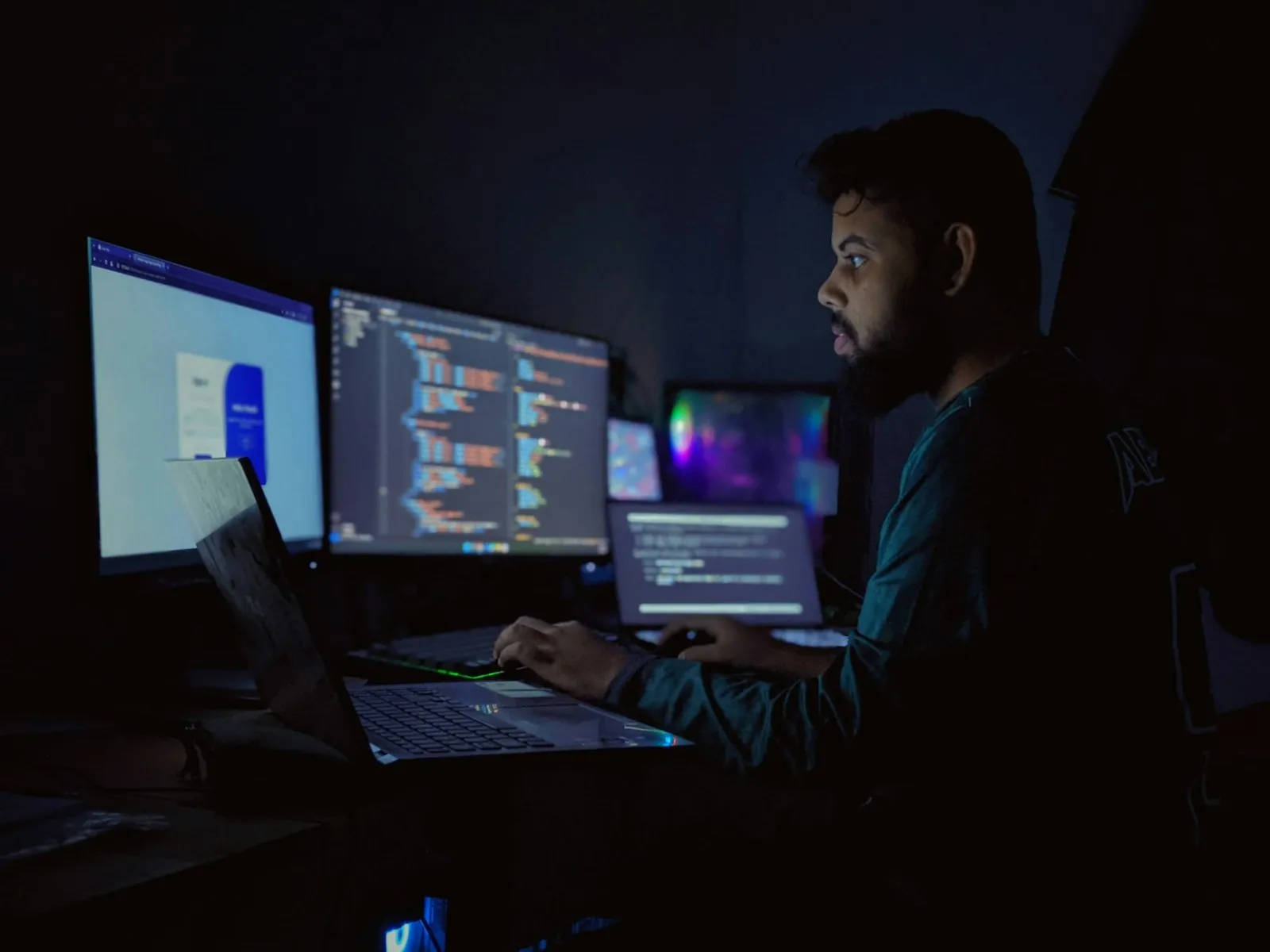 A developer coding at night in front of a three-monitor desk setup