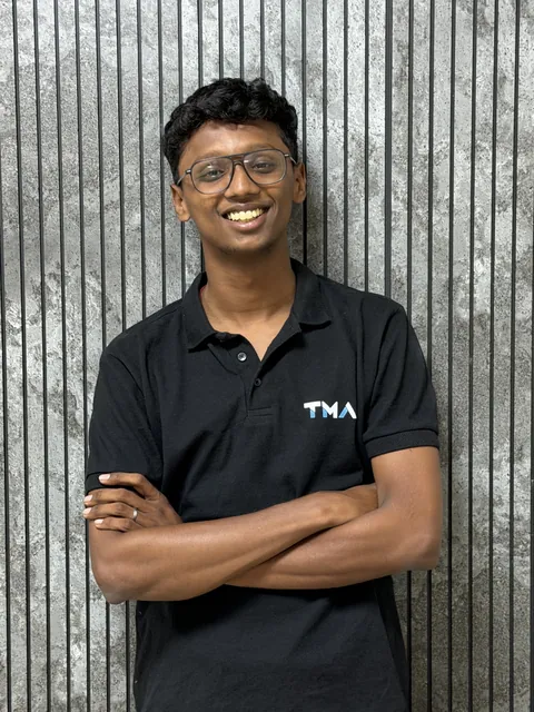 Rahul Dhileep Kumar smiling in a Track My Academy polo against a grey slatted wall